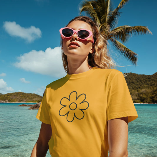 Woman wearing a Qurrito yellow floral graphic t-shirt with a bold flower design, styled with pink sunglasses, standing near the ocean under a palm tree.