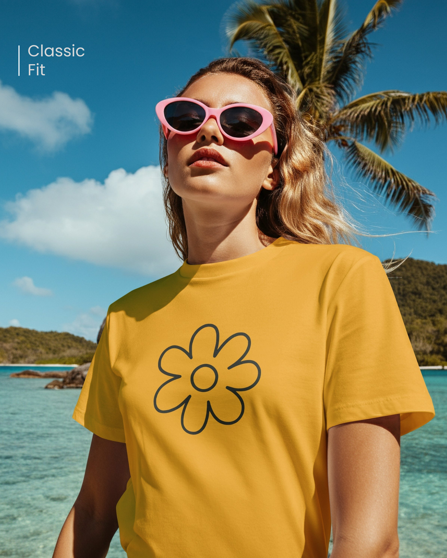 Woman wearing a Qurrito yellow floral graphic t-shirt with a bold flower design, styled with pink sunglasses, standing near the ocean under a palm tree.