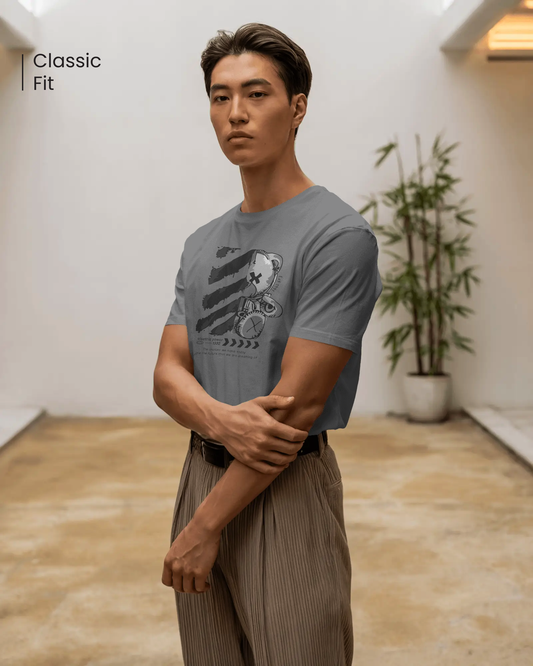 Male model wearing the bold and confident mood Qurrito's Goth Teddy T-Shirt in gray, featuring a futuristic and dark graphic. This classic fit men's t-shirt is styled for a modern streetwear look with pleated chinos.