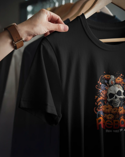 Detail closeup of the dark "Reborn" T-shirt with a playful skull and orange pumpkin illustration. Hand pulling tee from rack. Gothic Qurrito brand.