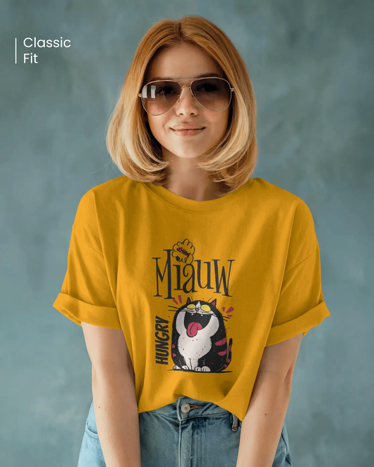 Qurrito Level 100 Hangry graphic t-shirt in an oversized fit worn by a woman with blonde hair and sunglasses. The mustard yellow tee features an Energetic Funny Graphic print of a wide-mouthed, black and white cat yelling "Miauw" and "HUNGRY." Energetic mood.