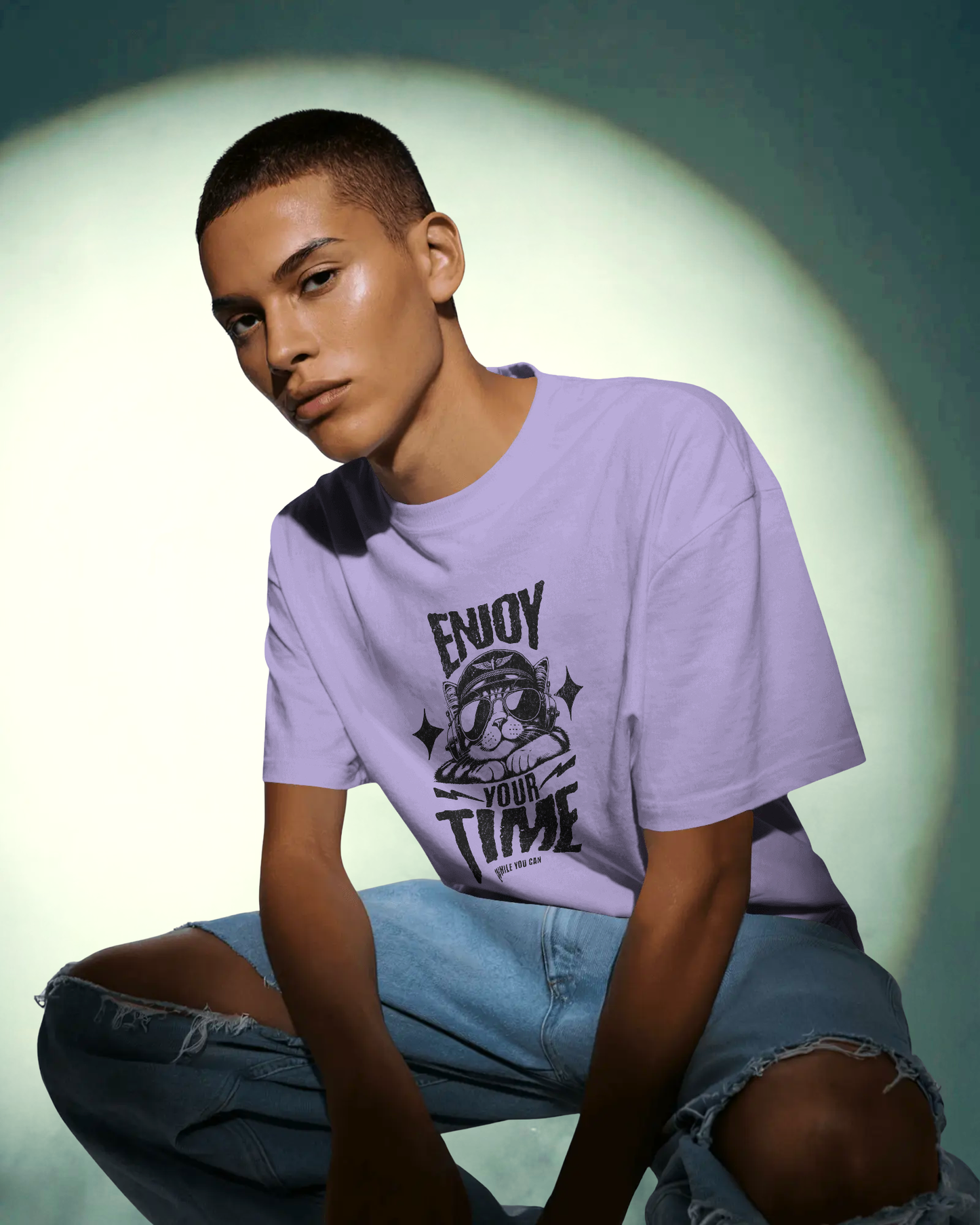 Man styling the Live in the Moment Oversized T-Shirt by Qurrito in lavender, paired with ripped blue jeans. The cool cat graphic gives it a playful yet chill vibe, ideal for men’s casual streetwear fashion.