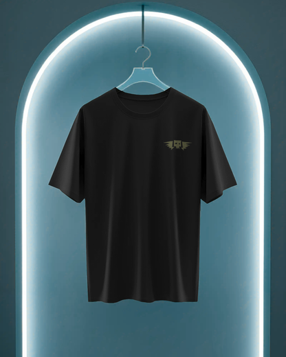 Qurrito’s Black Oversized T-Shirt featuring a minimal embroidered winged skull design hanging under neon lighting. The clean, dark aesthetic embodies mystery and bold streetwear appeal, perfect for unisex oversized fashion.