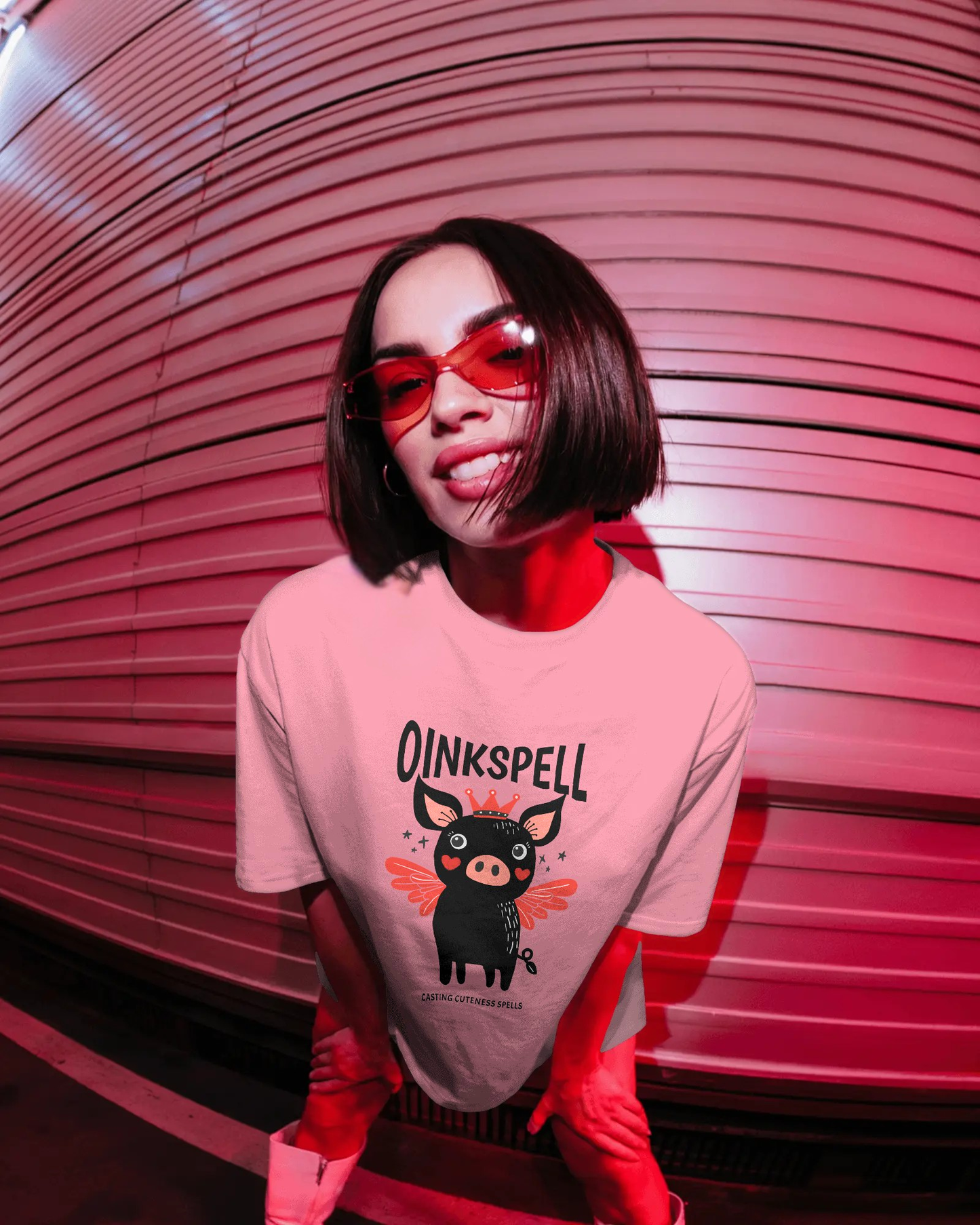 Woman wearing Qurrito’s Oinkspell Quirky Oversized T-Shirt in pink, paired with white sneakers and tinted glasses for a playful, fun, and cheerful mood street look, ideal for women’s casual graphic streetwear fashion.
