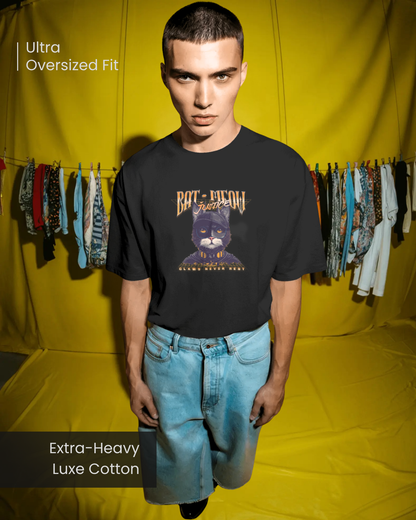 Male model in an Ultra Oversized Fit black T-shirt made from Extra-Heavy Luxe Cotton. The tee displays a quirky "Bat-Meow Justice" graphic with "Claws Never Rest." Ideal unisex graphic tee for a playful and comfortable streetwear style.