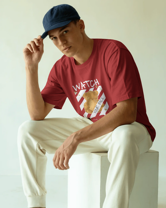 Red oversized t-shirt featuring a teddy bear graphic facing away with the bold text 'Watch Your Back,' safety pin details, and diagonal caution stripes. Includes the phrase 'Real world is behind your back' at the bottom. Urban graphic wear style by Qurrito.