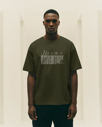Man wearing a green travel inspired t-shirt with 'Life is an Adventure' text against a plain background