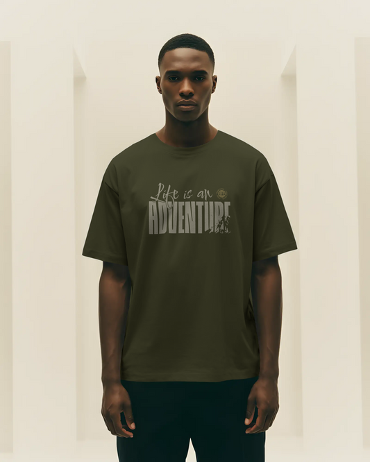 Man wearing a green travel inspired t-shirt with 'Life is an Adventure' text against a plain background