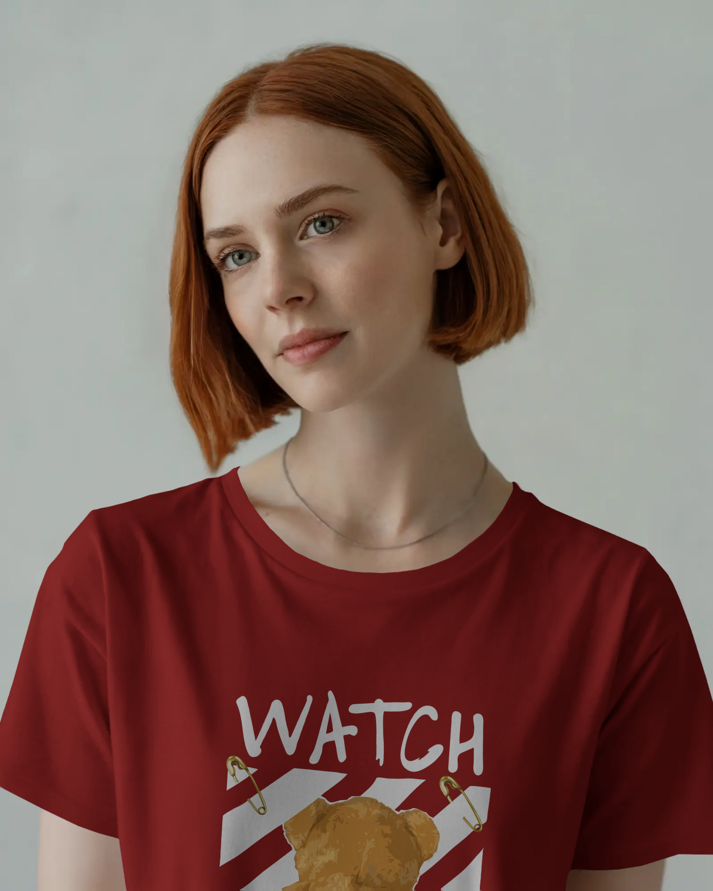 Red oversized t-shirt featuring a teddy bear graphic facing away with the bold text 'Watch Your Back,' safety pin details, and diagonal caution stripes. Includes the phrase 'Real world is behind your back' at the bottom. Urban graphic wear style by Qurrito.