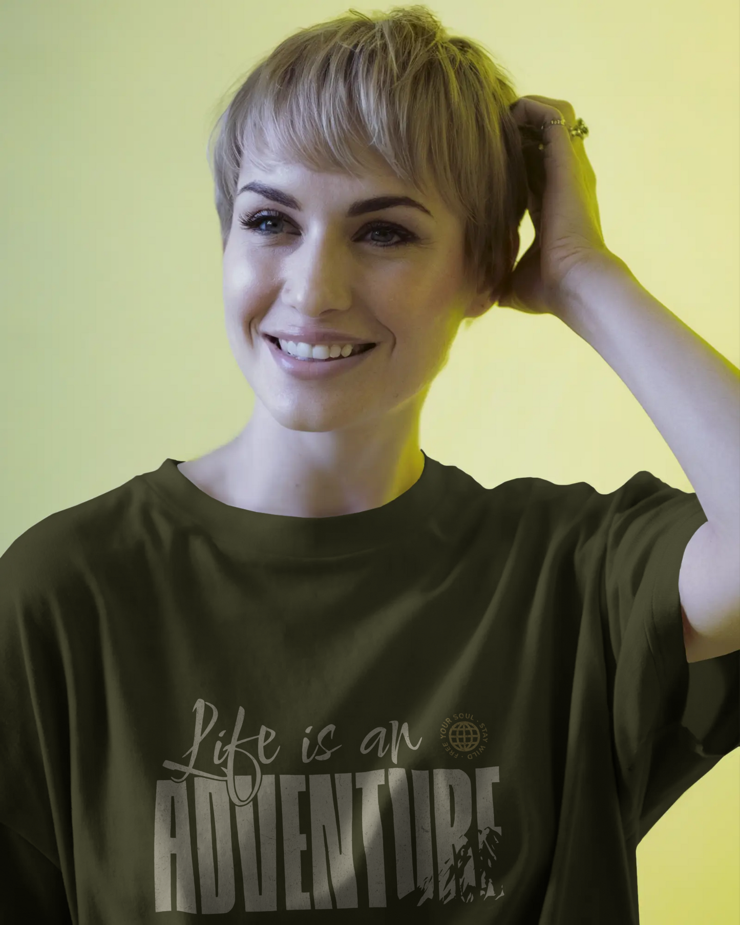Woman wearing a dark green travel inspired t-shirt with 'Life is an Adventure' text against a yellow background