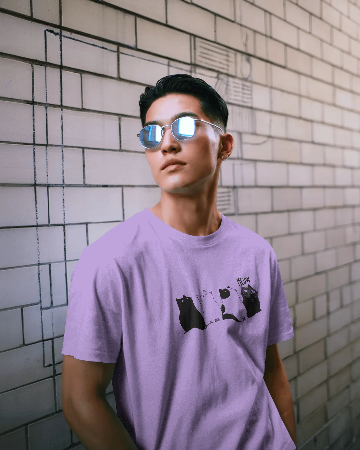 Qurrito The Purr-ple Squad graphic t-shirt in Classic Fit worn by a man against a brick wall. The Lilac tee features a Chill Cat Graphic of four cats. Chill mood.