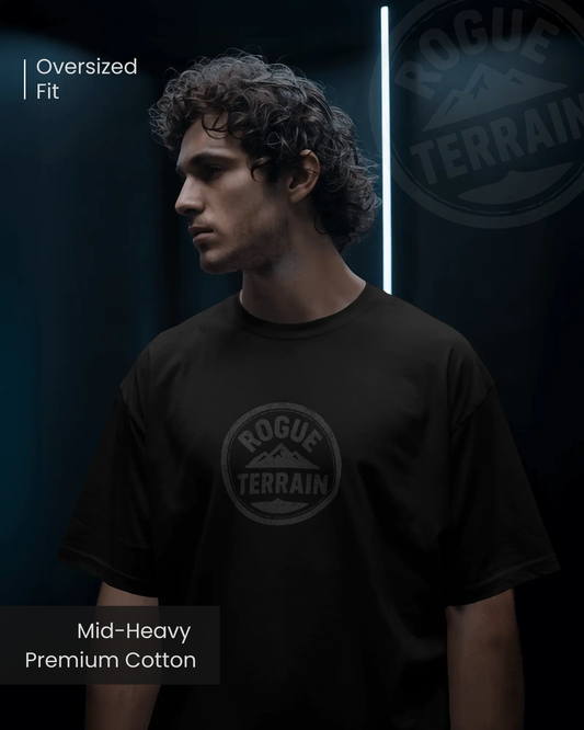 Male model wearing Qurrito’s Black Urban Outdoor T-Shirt with Rogue Terrain steel logo design. Crafted from mid-heavy premium cotton in an oversized fit, this minimalistic tee channels chill, relaxed, serious, and focused moods — perfect for modern streetwear and outdoor style.