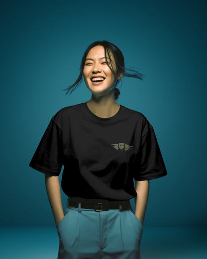 Woman wearing Qurrito’s Black Winged Skull Oversized Streetwear Tee tucked into blue high-waist pants. The subtle embroidery and dark tone project confidence and mystery mood, creating a bold yet minimalist streetwear outfit.
